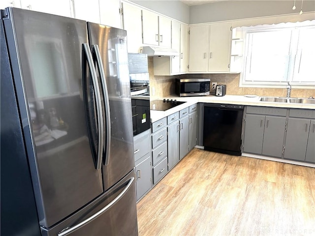 kitchen featuring light hardwood / wood-style flooring, sink, black appliances, gray cabinets, and tasteful backsplash