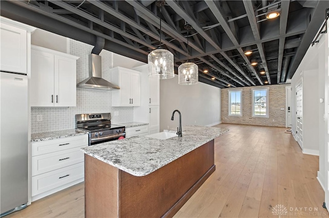 kitchen featuring appliances with stainless steel finishes, sink, wall chimney range hood, white cabinets, and an island with sink