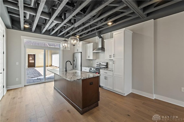 kitchen featuring a kitchen island with sink, light stone counters, appliances with stainless steel finishes, white cabinets, and wall chimney exhaust hood