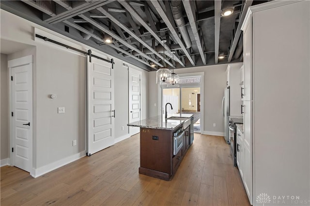 kitchen featuring a center island with sink, light stone counters, white cabinets, a barn door, and light wood-type flooring