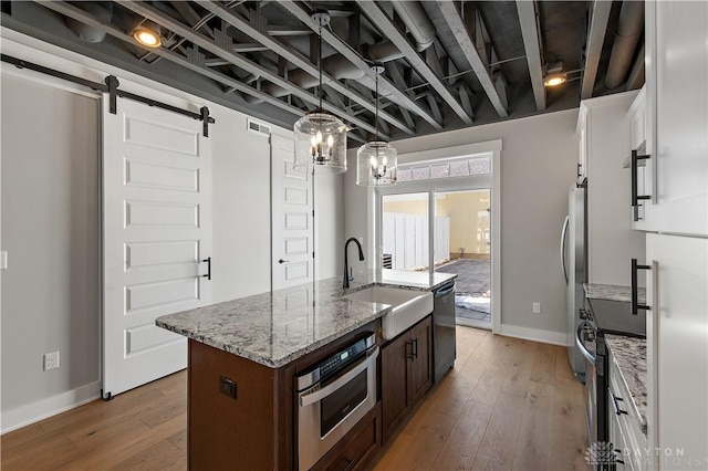 kitchen featuring an island with sink, stainless steel appliances, white cabinets, a barn door, and sink