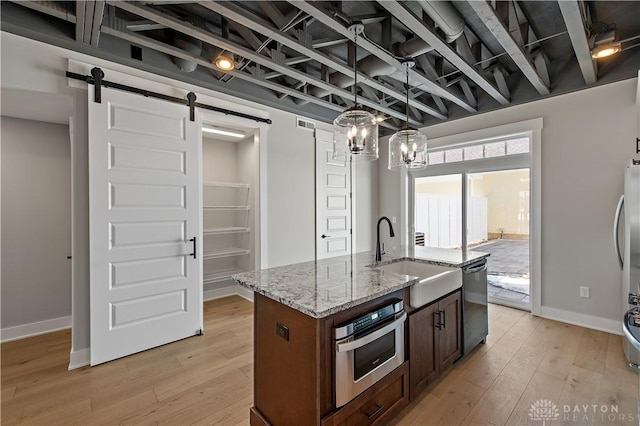 kitchen with stainless steel oven, a barn door, black dishwasher, light hardwood / wood-style floors, and sink