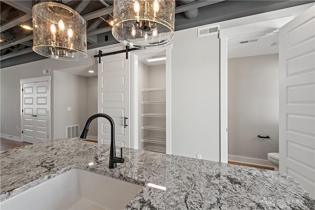 kitchen featuring a barn door, sink, hanging light fixtures, and light stone countertops