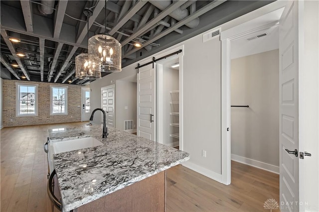 kitchen featuring brick wall, light hardwood / wood-style floors, light stone countertops, and a barn door