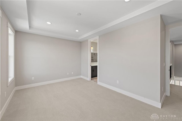 unfurnished bedroom with a tray ceiling, light carpet, and ensuite bath