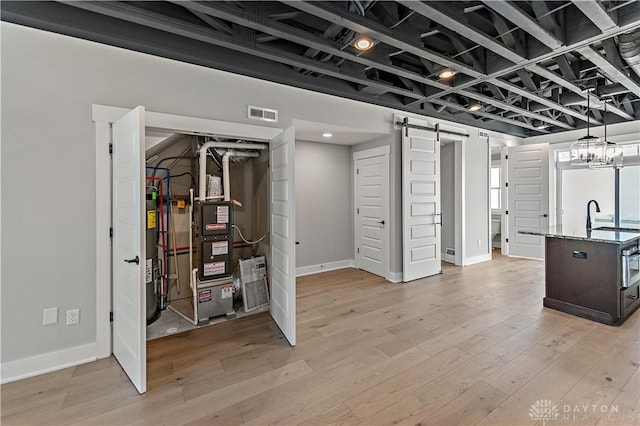 basement with heating unit, light hardwood / wood-style floors, sink, and a barn door