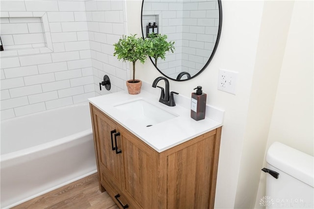 full bathroom featuring wood-type flooring, vanity, tiled shower / bath combo, and toilet