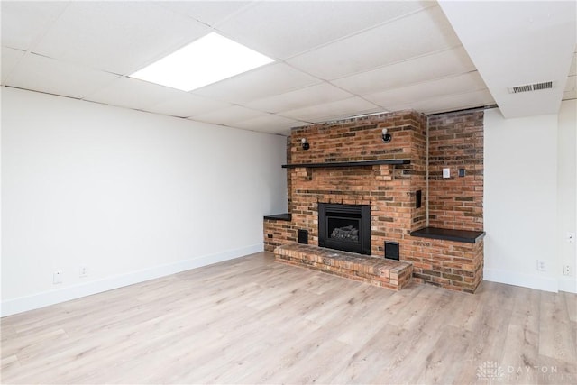 unfurnished living room featuring a drop ceiling, light wood-type flooring, and a brick fireplace