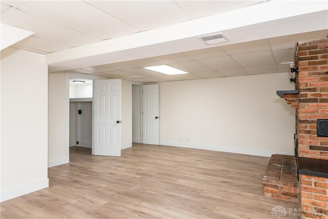 basement with a fireplace, light hardwood / wood-style flooring, and a paneled ceiling