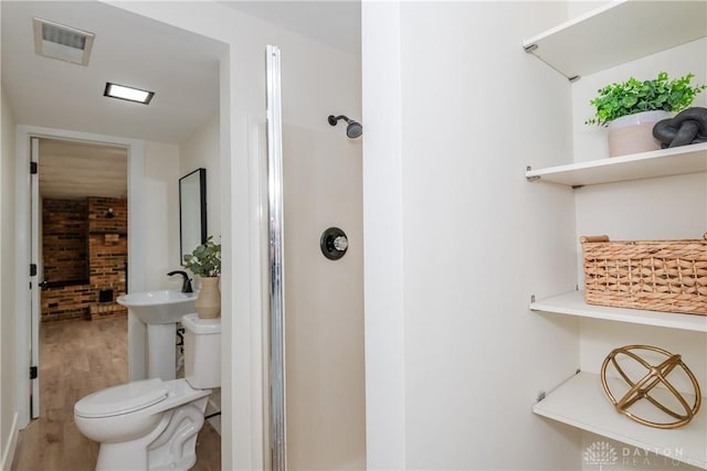 bathroom with toilet, brick wall, and wood-type flooring