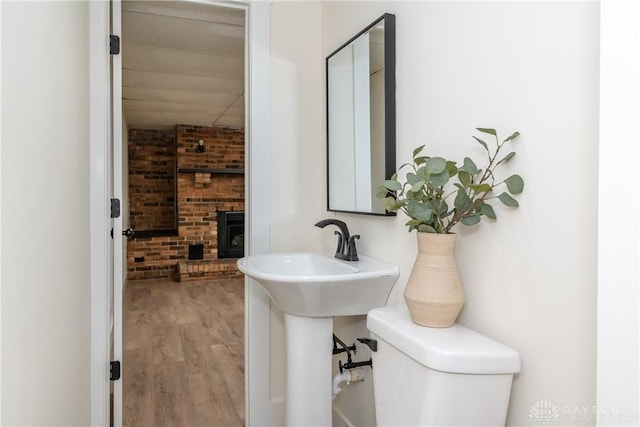 bathroom featuring sink, toilet, hardwood / wood-style floors, and brick wall