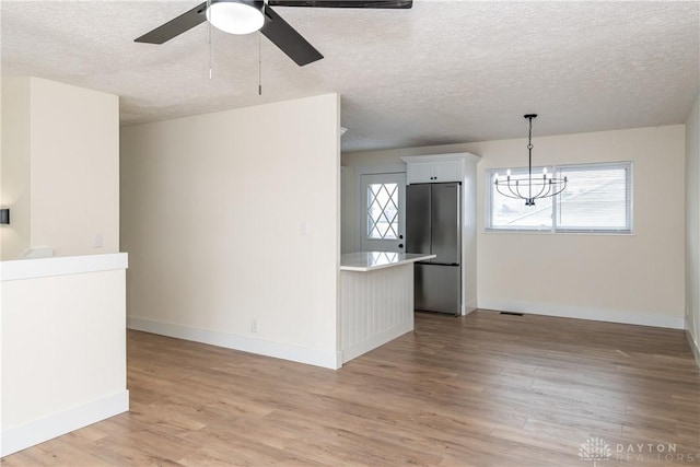 kitchen featuring white cabinetry, light hardwood / wood-style flooring, decorative light fixtures, stainless steel refrigerator, and a wealth of natural light