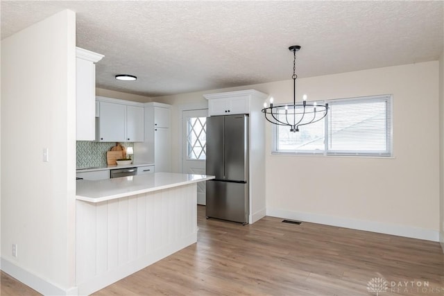 kitchen featuring light wood-type flooring, stainless steel appliances, hanging light fixtures, white cabinets, and decorative backsplash