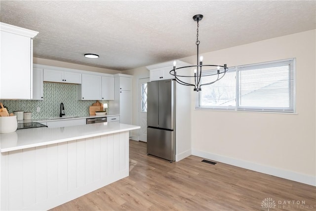 kitchen with hanging light fixtures, stainless steel appliances, light hardwood / wood-style floors, sink, and white cabinetry