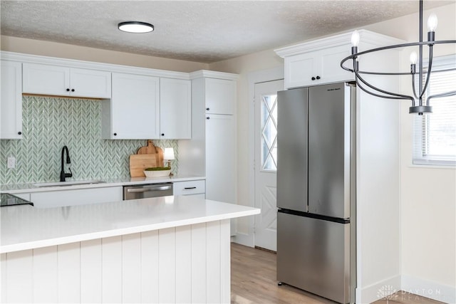 kitchen featuring light hardwood / wood-style floors, sink, appliances with stainless steel finishes, white cabinets, and pendant lighting