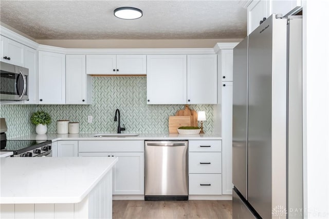 kitchen featuring stainless steel appliances, light hardwood / wood-style flooring, sink, tasteful backsplash, and white cabinets