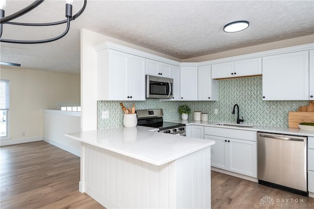 kitchen featuring stainless steel appliances, light hardwood / wood-style floors, sink, white cabinetry, and kitchen peninsula