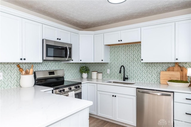 kitchen featuring light hardwood / wood-style flooring, sink, appliances with stainless steel finishes, white cabinets, and decorative backsplash