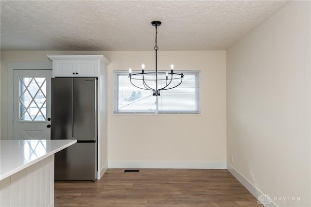 unfurnished dining area featuring a notable chandelier, light wood-type flooring, a textured ceiling, and a wealth of natural light