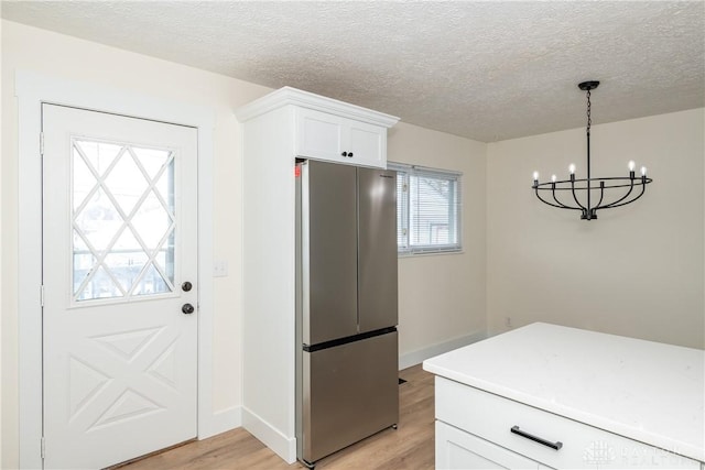 kitchen with light wood-type flooring, hanging light fixtures, white cabinets, and stainless steel fridge