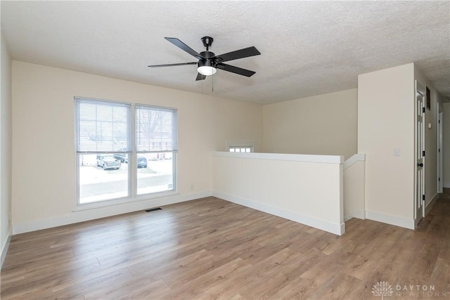 unfurnished room with ceiling fan, light wood-type flooring, and a textured ceiling