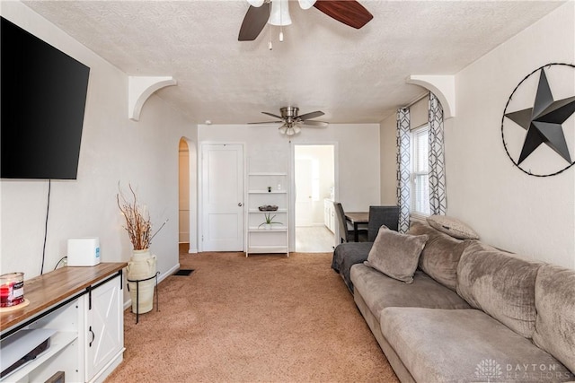 living room featuring ceiling fan, light carpet, and a textured ceiling