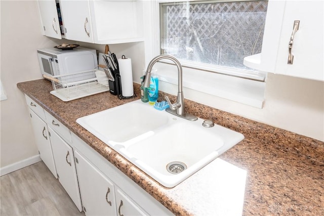 interior space with light hardwood / wood-style floors, white cabinetry, and sink