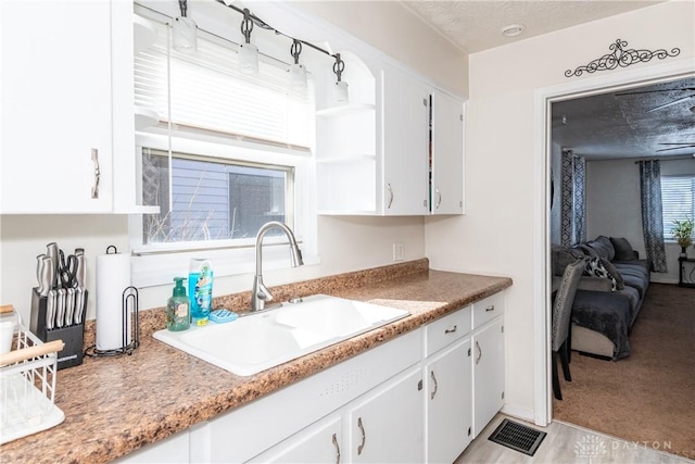 kitchen featuring sink, light carpet, white cabinets, and a textured ceiling