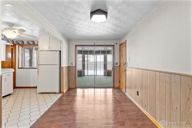 kitchen featuring white fridge, ceiling fan, a textured ceiling, white cabinets, and wooden walls