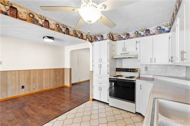 kitchen with electric stove, wooden walls, a textured ceiling, white cabinets, and sink