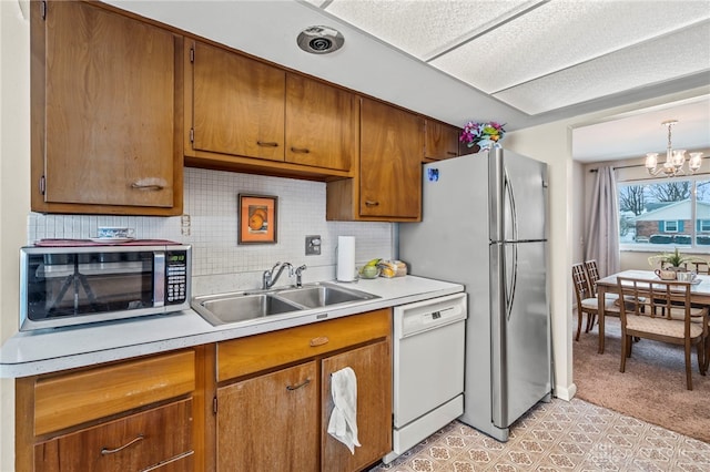 kitchen featuring appliances with stainless steel finishes, sink, backsplash, a notable chandelier, and hanging light fixtures