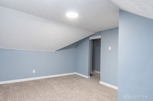 bonus room with a textured ceiling, lofted ceiling, and light colored carpet