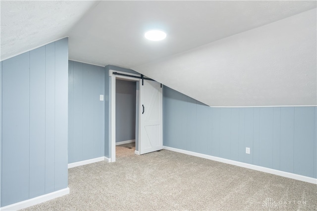 additional living space with a barn door, vaulted ceiling, and light colored carpet