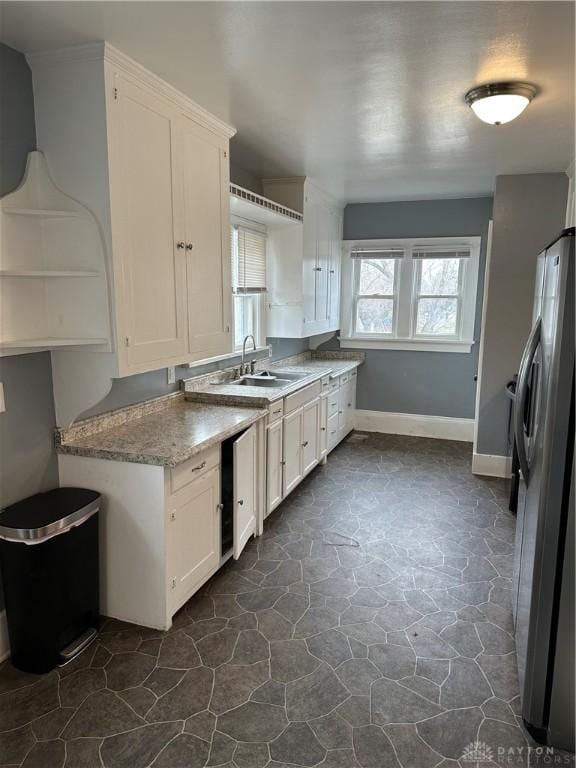 kitchen featuring white cabinetry, sink, stainless steel fridge, and light stone counters