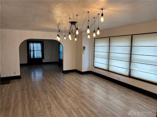 empty room with a textured ceiling, a notable chandelier, and dark hardwood / wood-style flooring