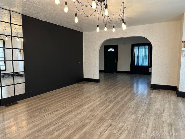 empty room featuring a textured ceiling, hardwood / wood-style floors, and an inviting chandelier