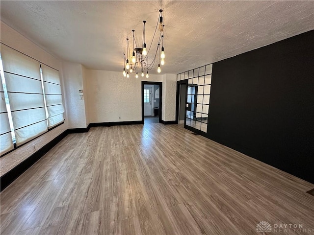 empty room featuring a textured ceiling, hardwood / wood-style floors, and a notable chandelier