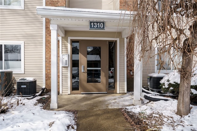 snow covered property entrance featuring central AC and brick siding