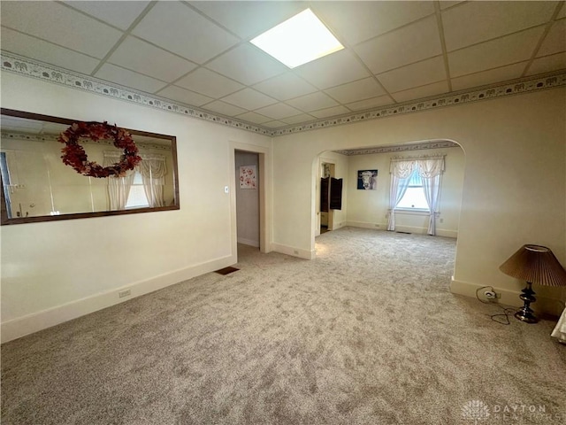 carpeted empty room featuring arched walkways, a paneled ceiling, and baseboards