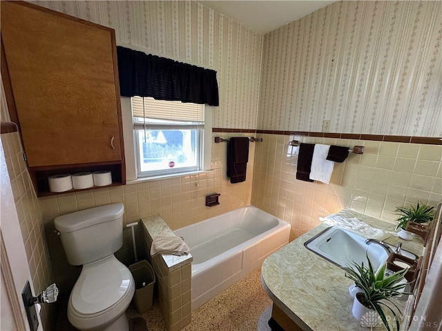 bathroom with a washtub, vanity, tile walls, and toilet