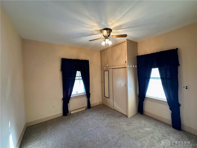 unfurnished bedroom with ceiling fan, multiple windows, carpet floors, and a baseboard heating unit