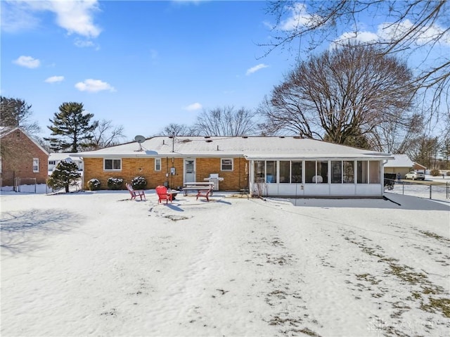 snow covered property with brick siding and a sunroom