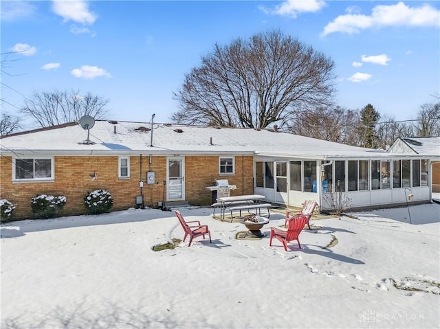 snow covered property featuring brick siding and a sunroom