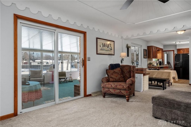 living area with baseboards, a ceiling fan, and light colored carpet