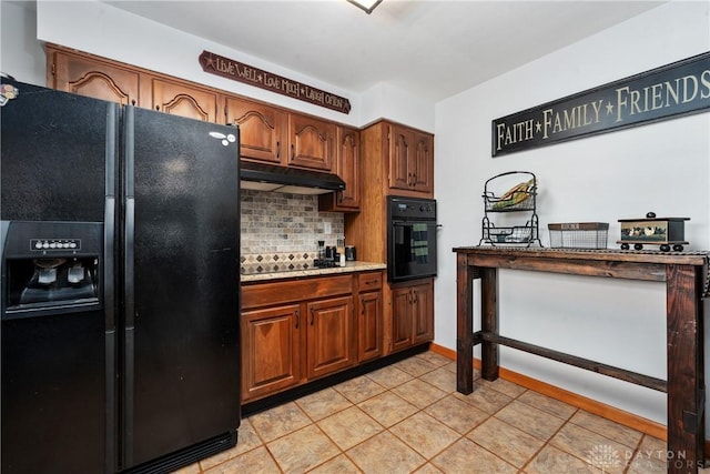 kitchen with light tile patterned floors, under cabinet range hood, light countertops, black appliances, and tasteful backsplash