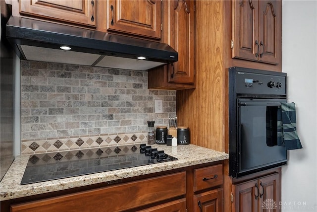 kitchen featuring extractor fan, brown cabinets, light stone countertops, black appliances, and tasteful backsplash