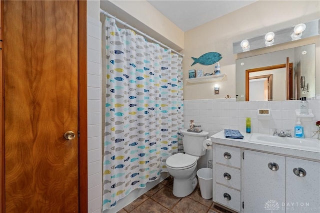 full bathroom with a wainscoted wall, tile walls, toilet, vanity, and tile patterned flooring