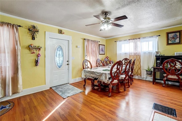 dining room featuring a textured ceiling, wood finished floors, visible vents, baseboards, and crown molding