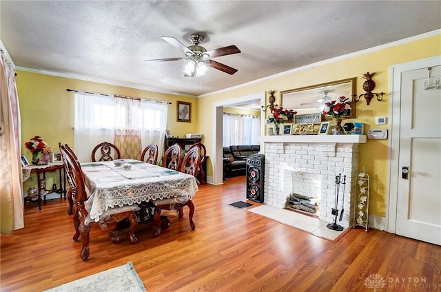 dining room featuring light wood-style floors, a fireplace, ornamental molding, and a textured ceiling