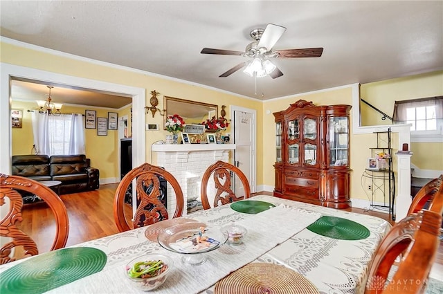 dining room with a fireplace, light wood-style floors, ornamental molding, baseboards, and ceiling fan with notable chandelier